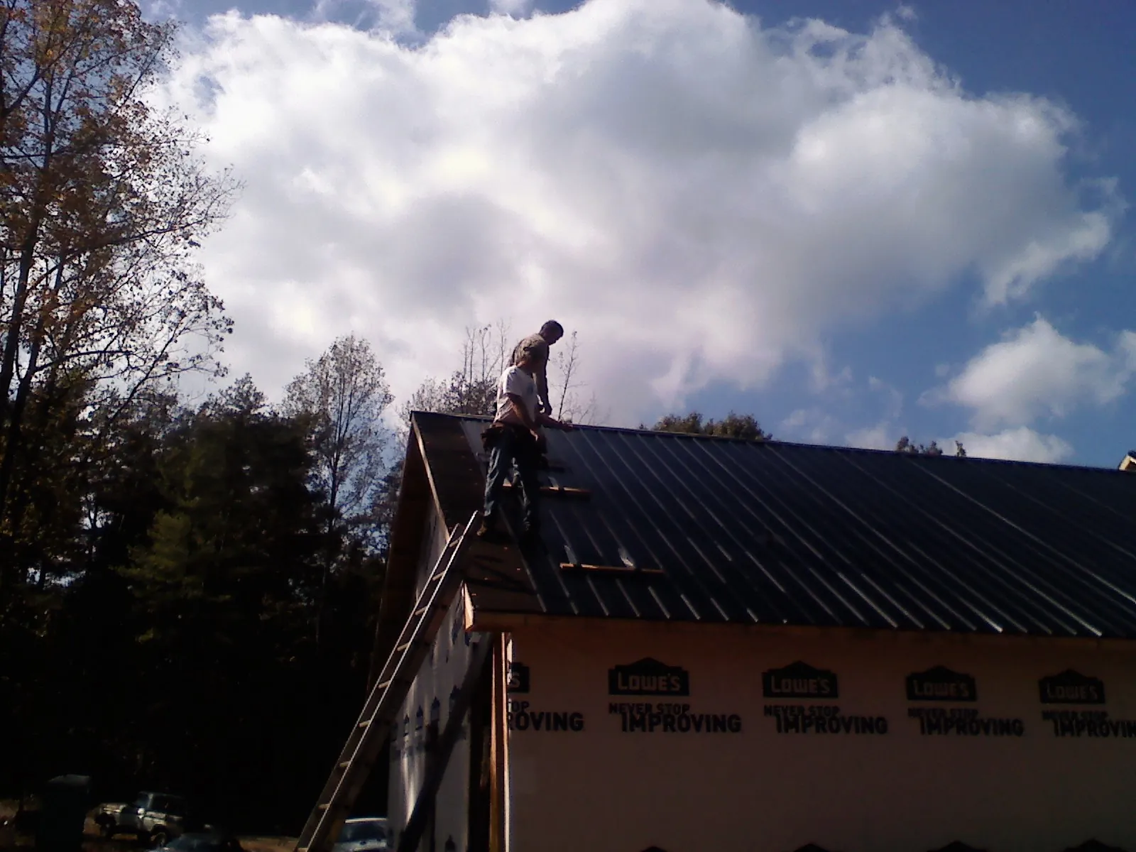 Roofer fastening dark metal panels high against a cloudy sky, from a Roof Inspection job in Seaside Park