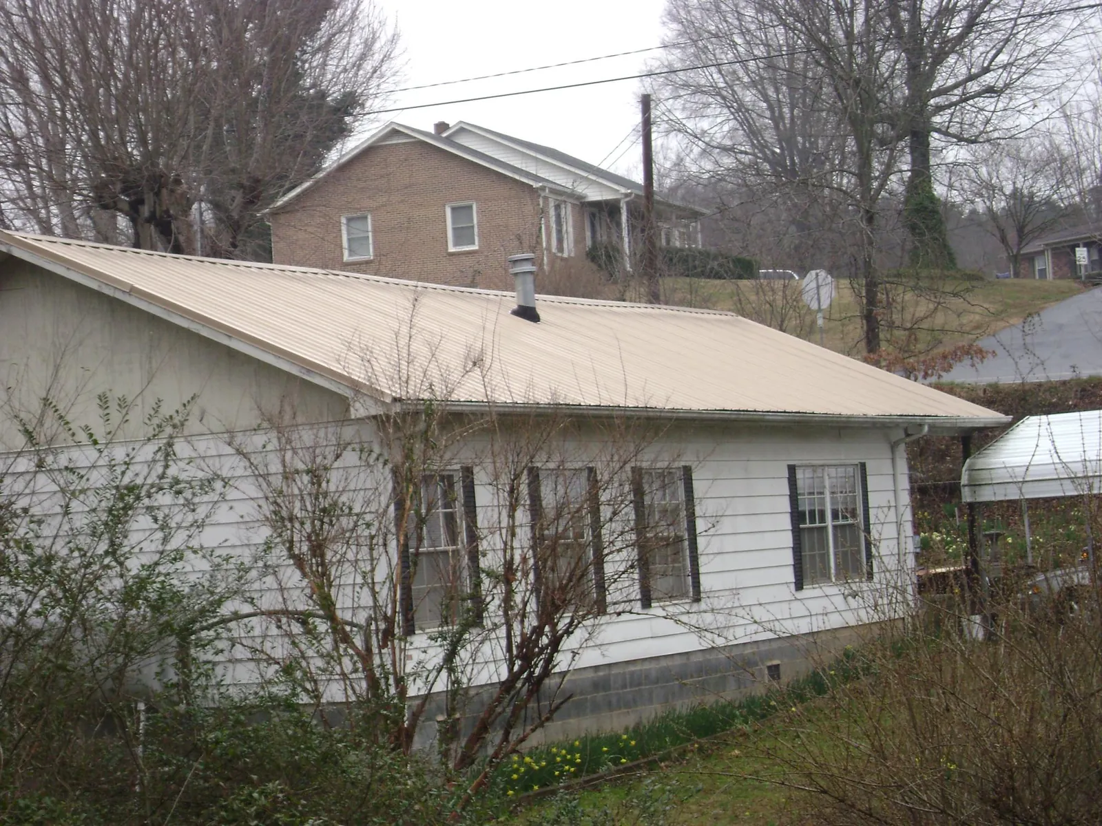 Tan metal roof on a white sided house set into a hillside — Commercial Roofing by Roofing Brothers in Seaside Park